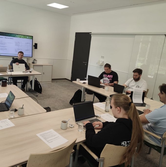 Das Bild zeigt eine Gruppe von Auszubildenden der kubus IT in einem modernen Seminarraum. Sie sitzen mit Laptops an Tischen und arbeiten konzentriert während eines Lehrgangs zur objektorientierten Programmierung. Im Hintergrund ist ein Dozent zu sehen, der Inhalte auf einem großen Bildschirm präsentiert. Die Atmosphäre wirkt fokussiert und praxisnah.