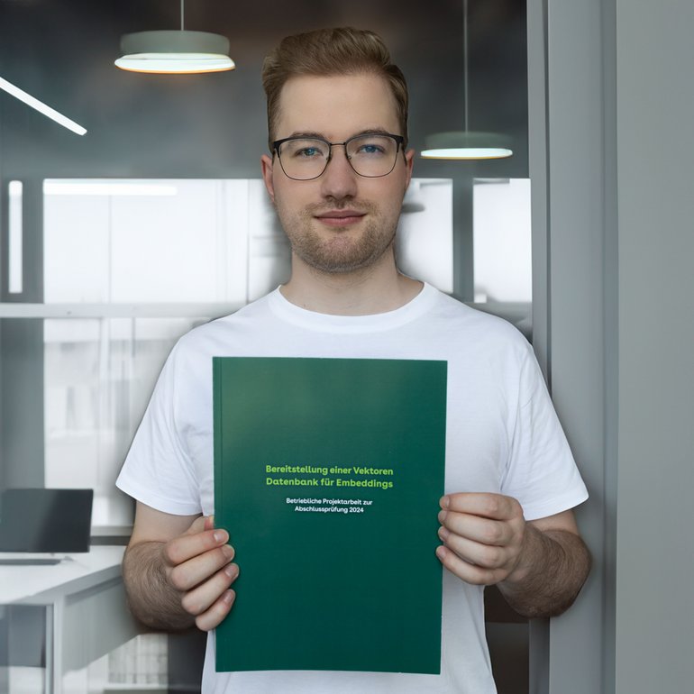 Ein Absolvent hält seine Abschlussarbeit in die Kamera