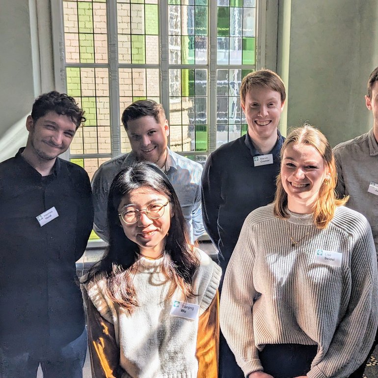 Die neuen Trainees des Jahrgangs 2024 stehen in einem Gebäude und schauen in die Kamera