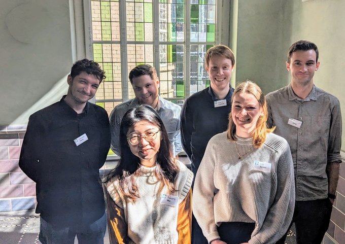 Die neuen Trainees des Jahrgangs 2024 stehen in einem Gebäude und schauen in die Kamera