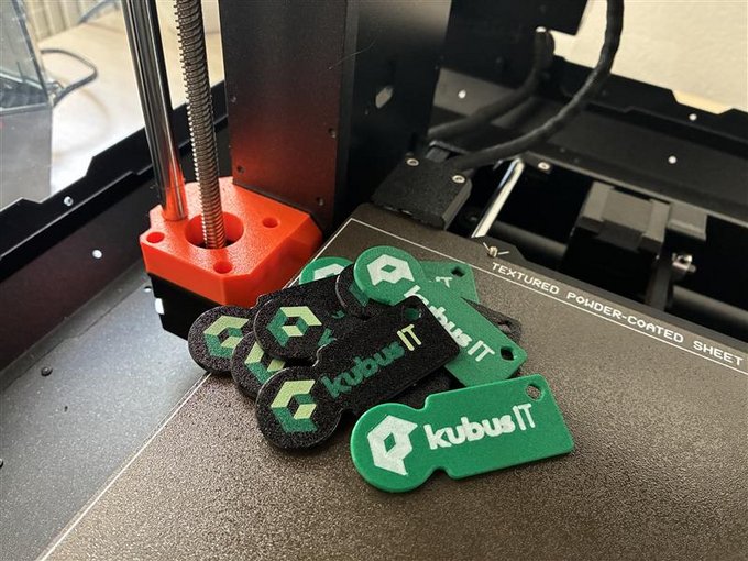 Mehrere grüne und schwarze Einkaufswagenchips mit kubus IT Logo liegen auf der Druckplatte eines 3D-Druckers.