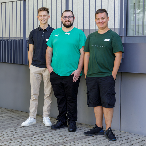 Drei junge Männer stehen vor dem Bildungsstandort in Gera und lächeln in die Kamera.