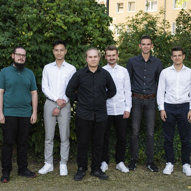 6 Auszubildende und Studierende stehen vor einer Hecke
