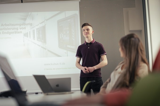 junger Mann hält eine Präsentation mithilfe eines Beamerbildes vor mehreren Personen im IT Gesundheitswesen | kubus IT GbR