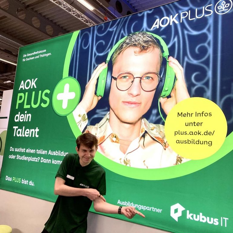 Ein Auszubildender zeigt auf das Logo der kubus IT auf einem Banner