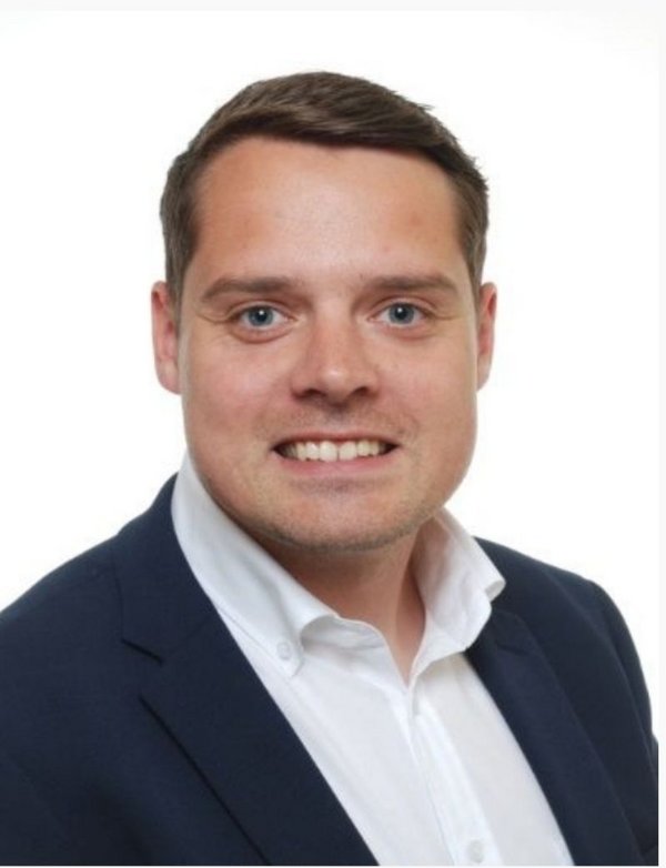 Das Bild zeigt Tom Blumenstein, den neuen Ausbildungsleiter der kubus IT. Er trägt ein Hemd, lächelt freundlich in die Kamera und steht vor einem neutralen Hintergrund.