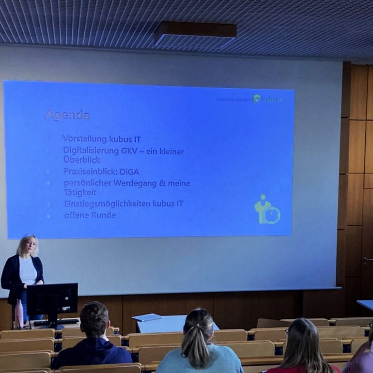 Eine Mitarbeiterin steht vor Studierenden in einem Hörsaal und stellt ihre Agenda vor